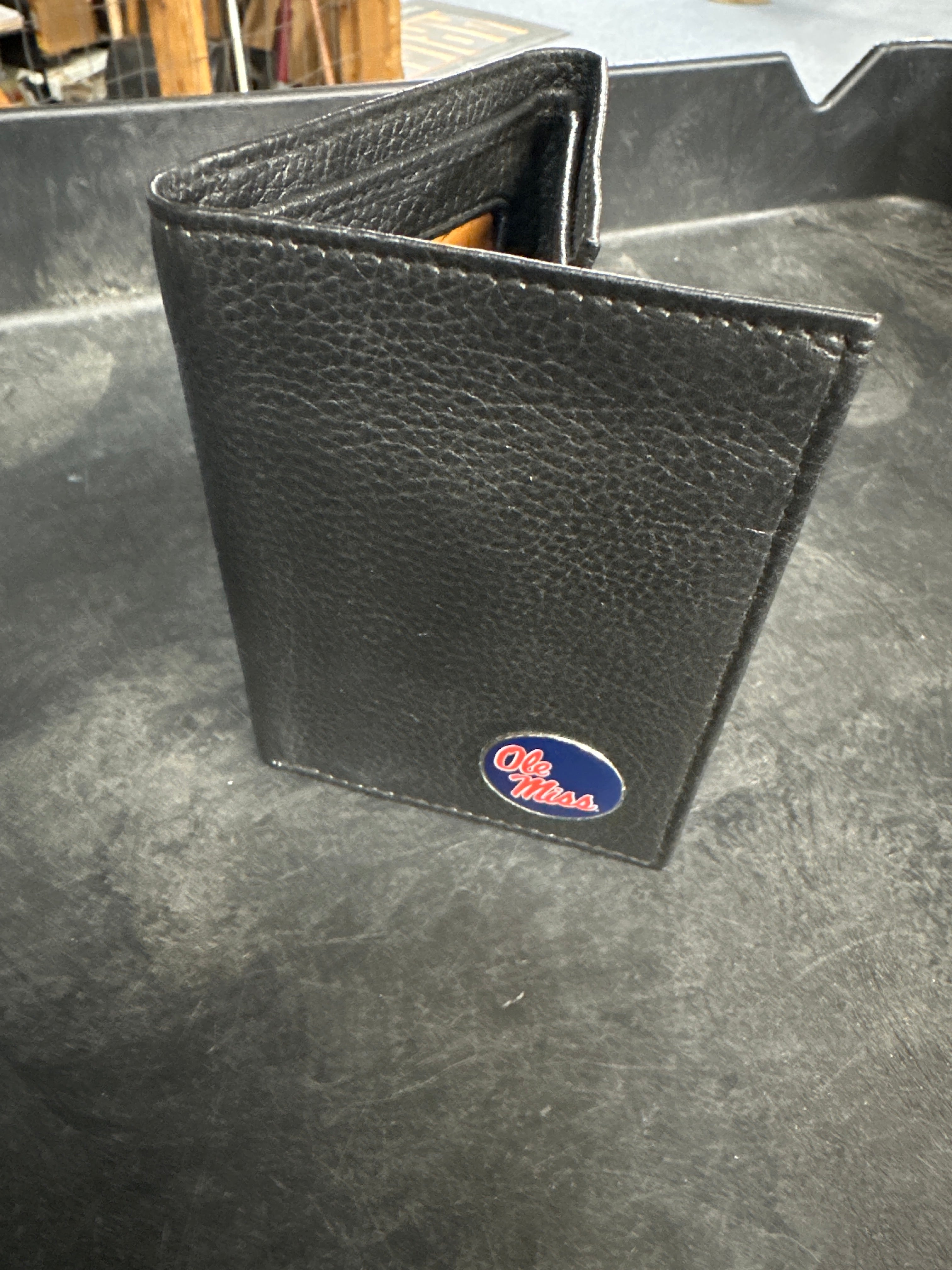 Black leather wallet with a logo on a metallic surface