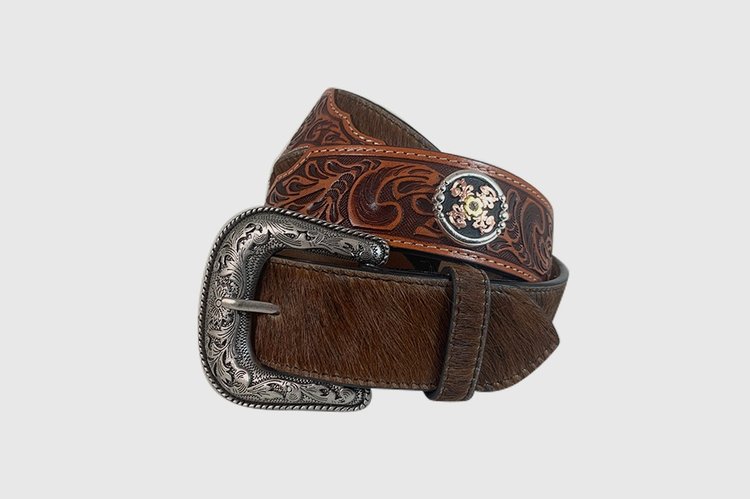 A brown hair-on leather belt with hand tooled designs and two conchos, featuring a silver finish buckle.