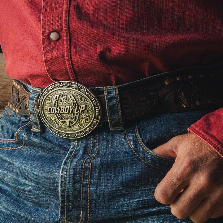 Belt buckle with 'Cowboy Up' text over a Horseshoe and a barbwire decorative pattern border. View on model