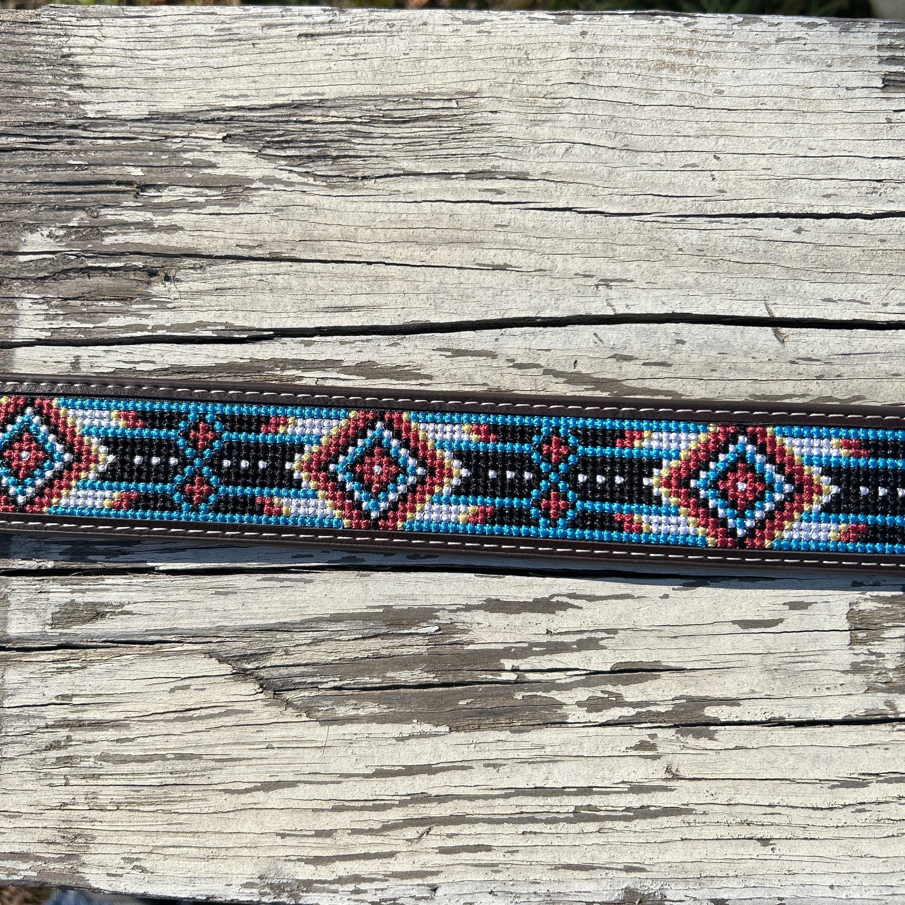 This Red and Blue embroidered belt has a basketweave leather overlay on each end with a matching keep. The Silver buckle has a intricate design featuring a Longhorn. Close up view of pattern.