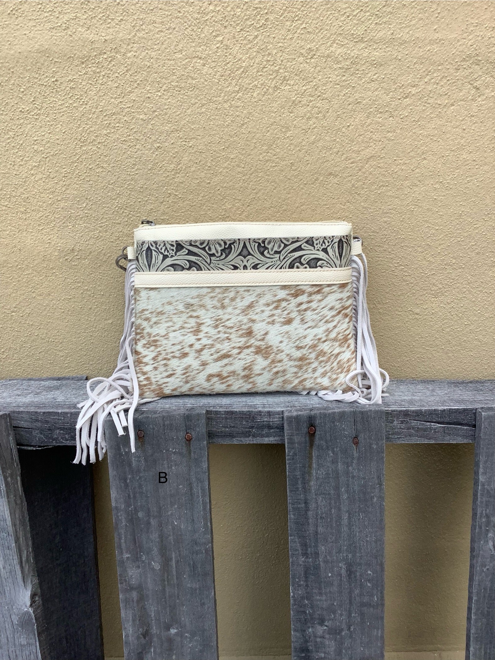 This cowhide and tooled leather crossbody bag features fringe sides and zips closed. The strap is removable and adjustable. Front View B