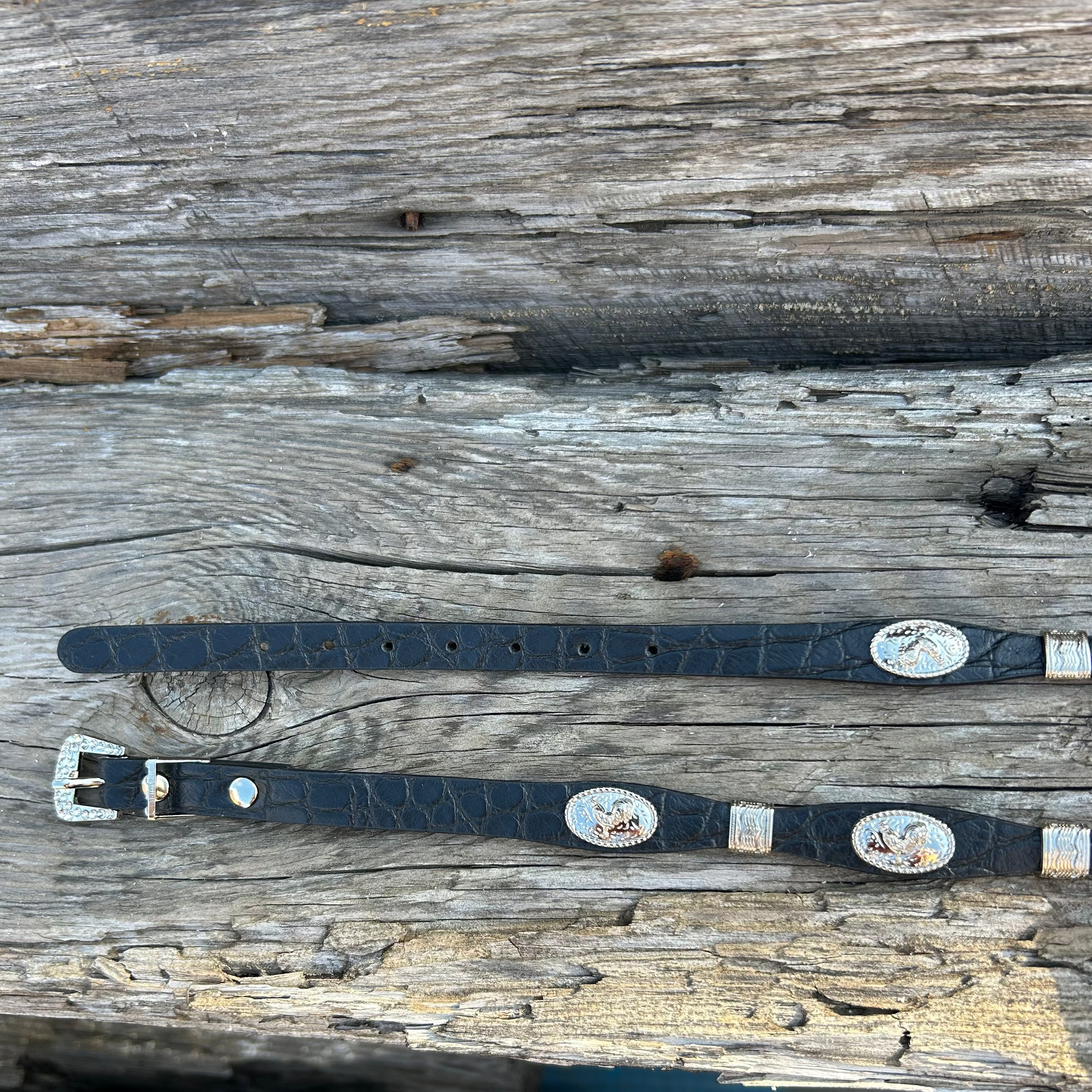This Black leather western style hat band features Silver Rooster Conchos with Silver bands in between. It has a adjustable fit with a crystal studded western style buckle for closure.