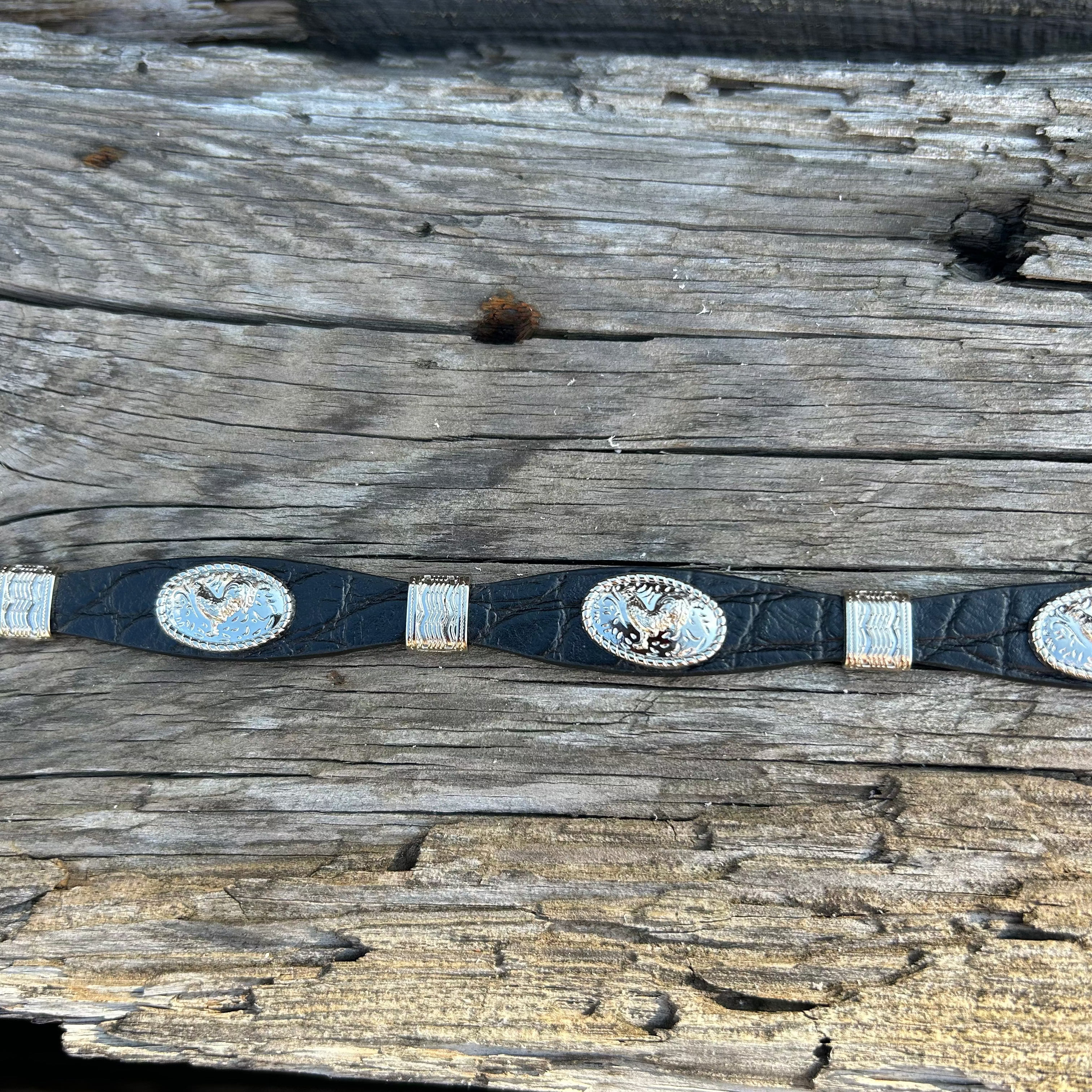 This Black leather western style hat band features Silver Rooster Conchos with Silver bands in between. It has a adjustable fit with a crystal studded western style buckle for closure. Close up view of Rooster Conchos and Silver Bands.