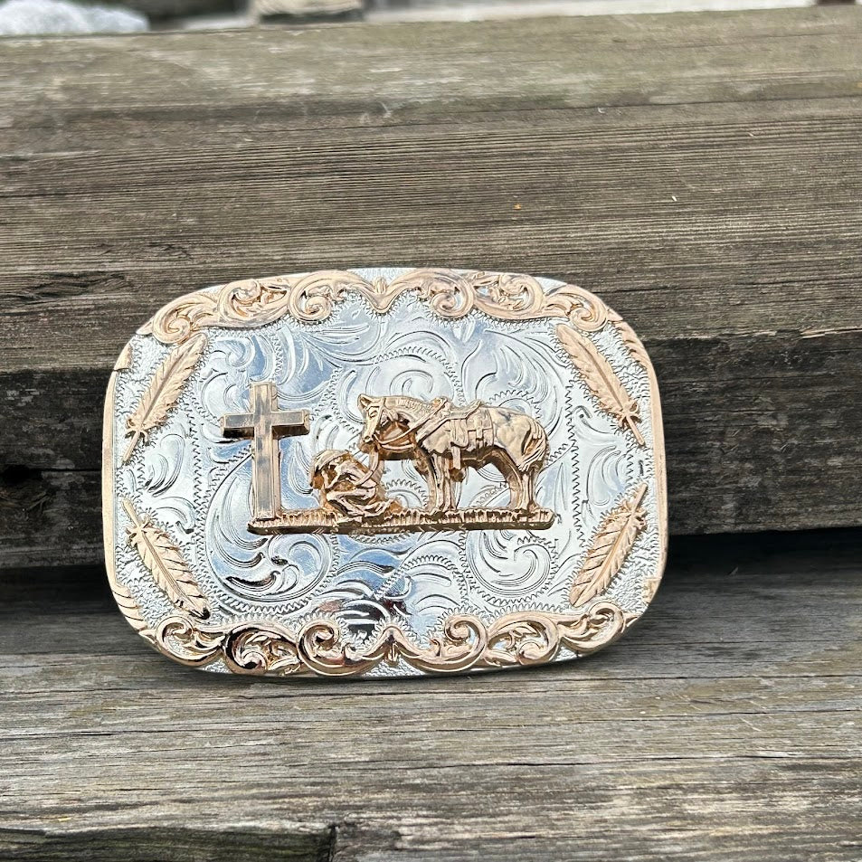 Silver rectangle belt buckle with a gold Praying Cowboy design. Buckle has a gold border with feathers. Front View