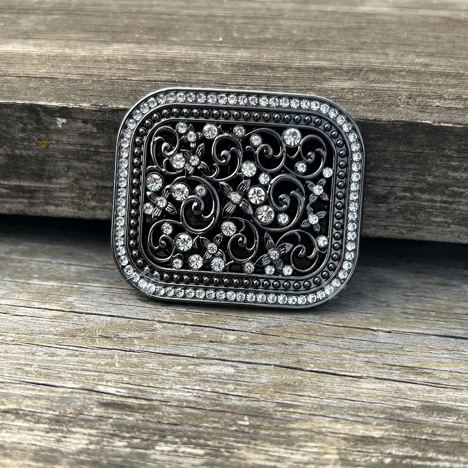 This matte black buckle features a floral scrollwork pattern with rhinestone accents and a rhinestone border. Front View