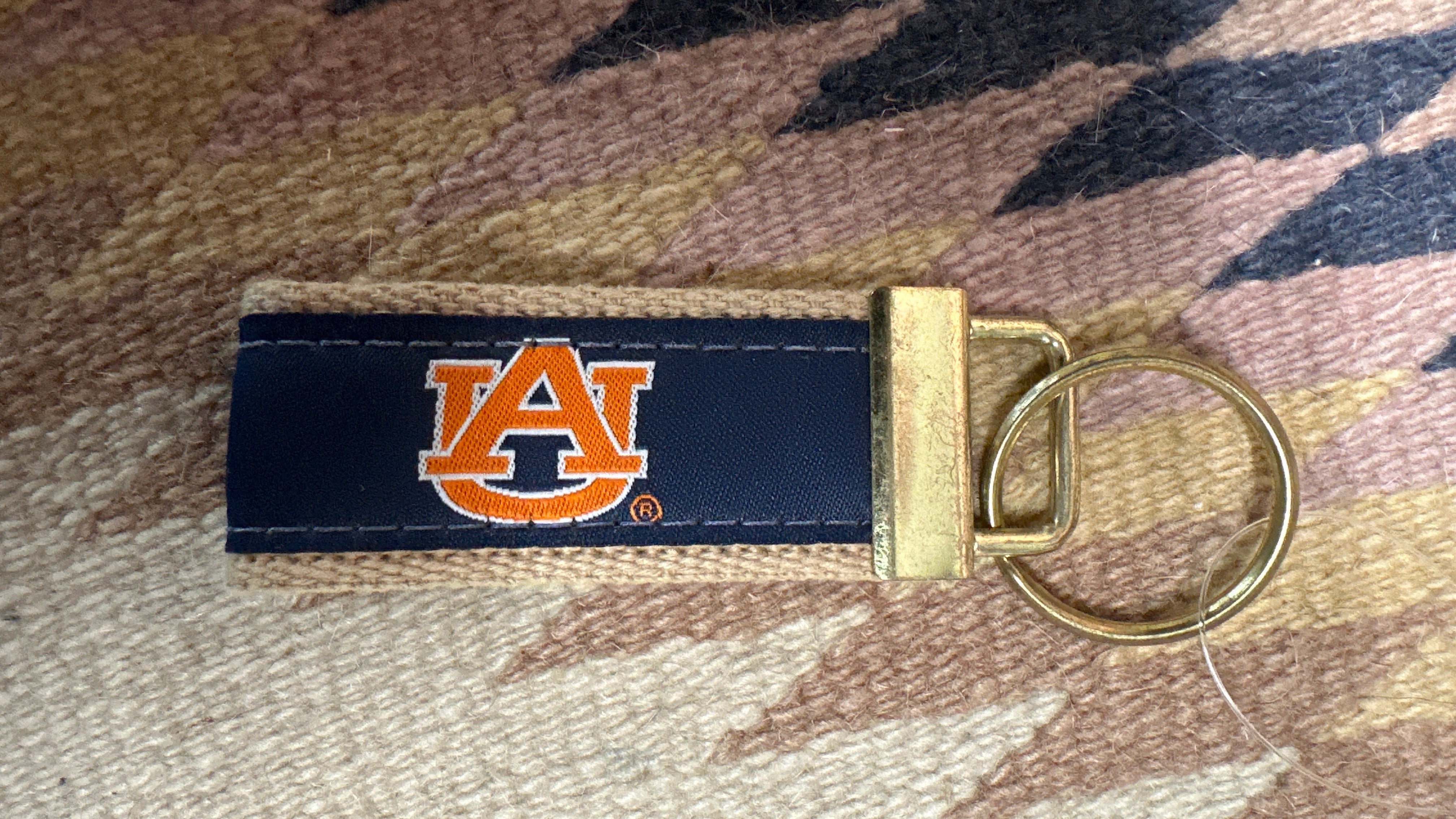 Front of Zep-Pro AU ribbon key fob showing embroidered orange logo on blue ribbon sewn to burlap strap. Attached by brass finish metal connector to round key ring.