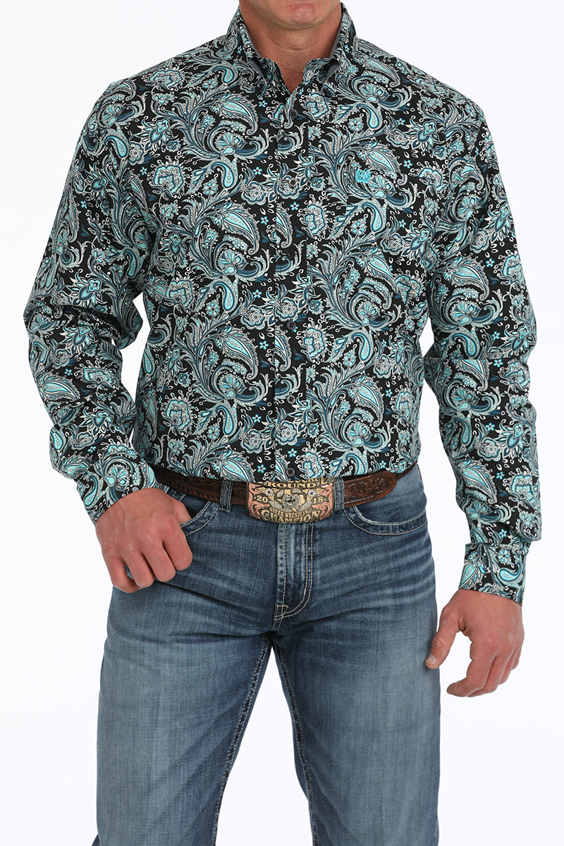 Man wearing a Cinch button down long sleeve black/turquoise/white paisley shirt with jeans, a belt and belt buckle. Front view.