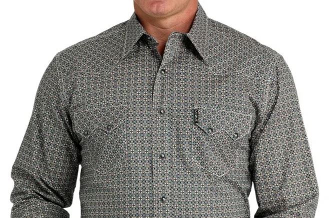 Close up of a man wearing a Cinch long sleeve snap shirt in an all-over gray print showing two-pocket detailing with sawtooth pocket flaps with snaps closures, shoulder yokes, and an open collar. Front view.
