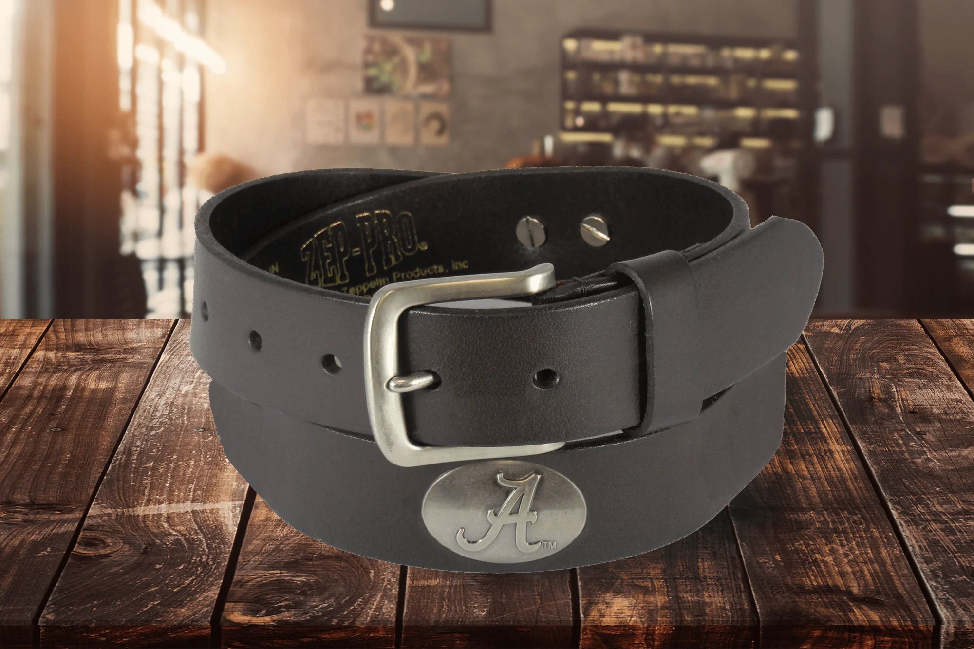 A Zep-Pro brown leather belt rolled up to show a silver metal buckle and an oval Alabama logo "A" silver tone concho.