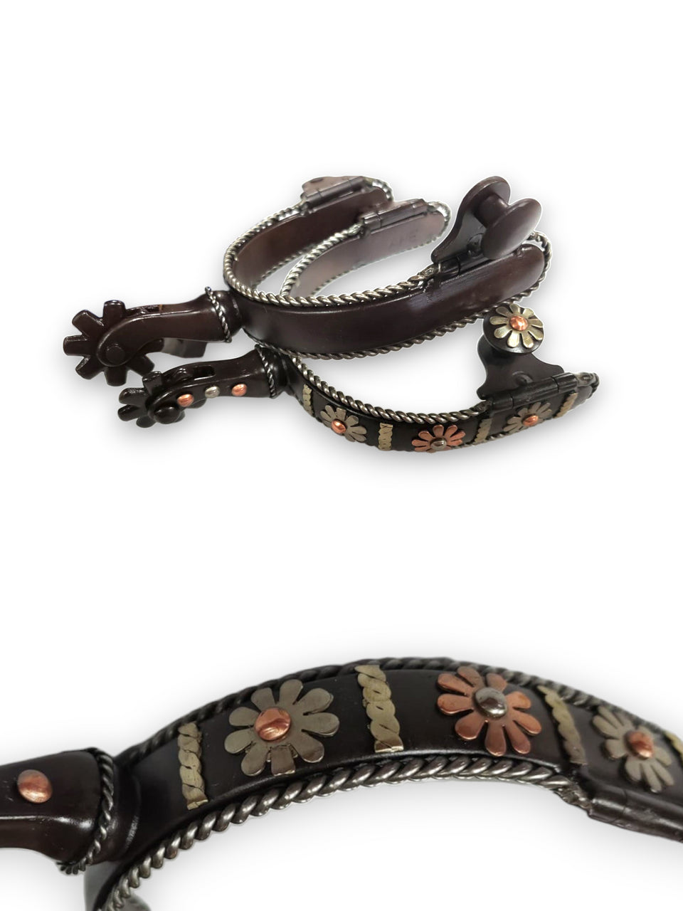 A pair of women's black steel spurs featuring a intricate copper flower design on outside band and shank with black steel blunt 8-point rowel. Silver steel rope edge lines bands and base of shanks.