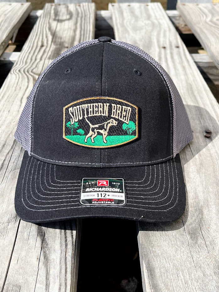 A black and gray Southern Bred cap with a logo on the front, placed on a wooden surface.