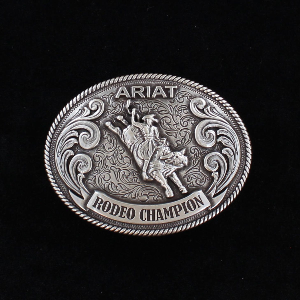 A youth sized silver tone oval belt buckle with a bull rider motif and the text 'ARIAT RODEO CHAMPION' engraved on it.