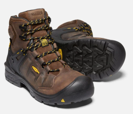 Keen Men's Dover 6 inch waterproof boots with carbon-fiber toe in dark earth and black. The boots have lace-up closure and a rubber outsole. Front view showing American Built tag and bottom outsole view of other boot.