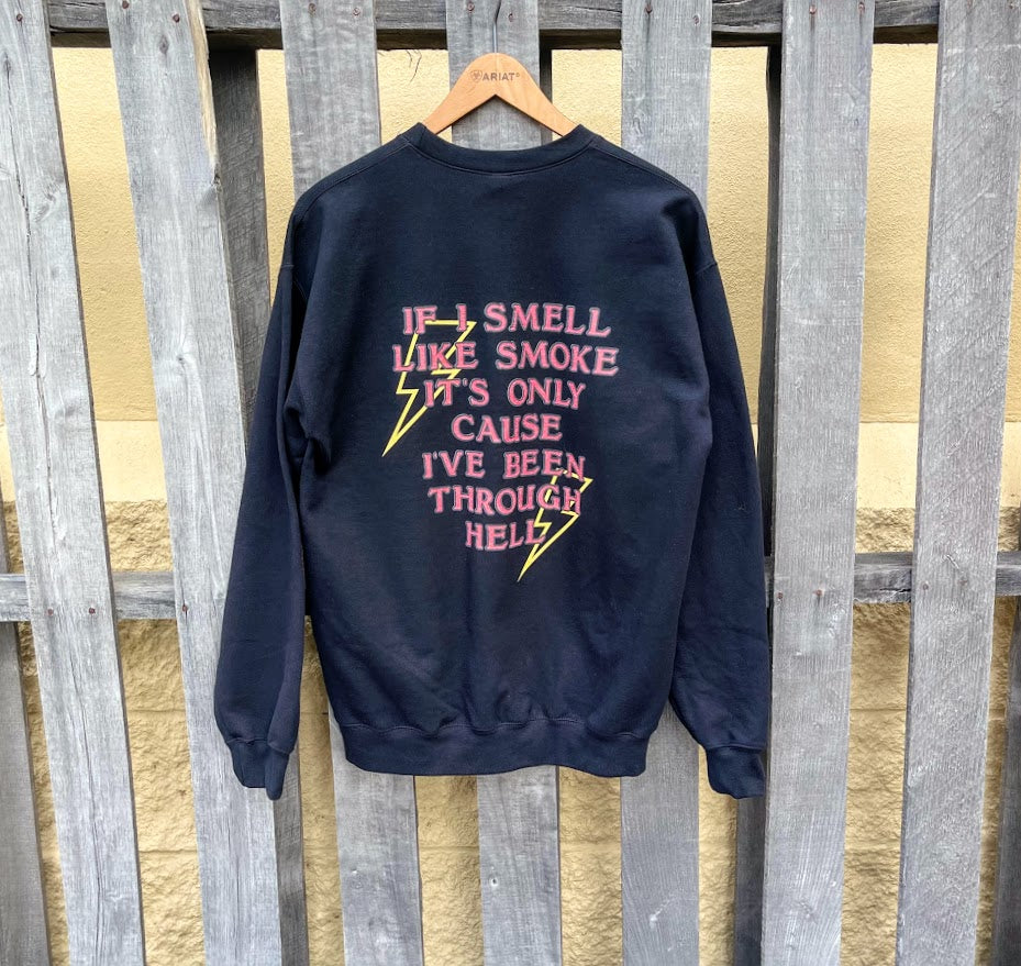 Black graphic sweatshirt that has red block print over 2 short lightning bolts. It reads: IF I SMELL LIKE SMOKE IT'S ONLY CAUSE I'VE BEEN THROUGH HELL. Back view.