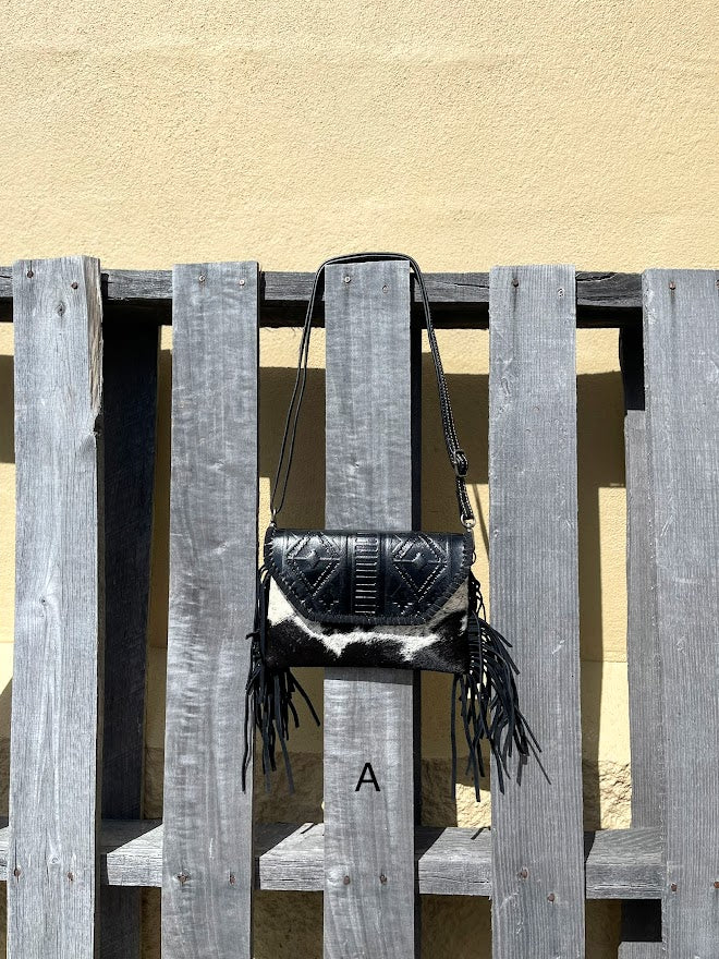 This cowhide and black leather crossbody bag has fringe sides. It features a whipstitch flap closure with a geometric design. Front View A