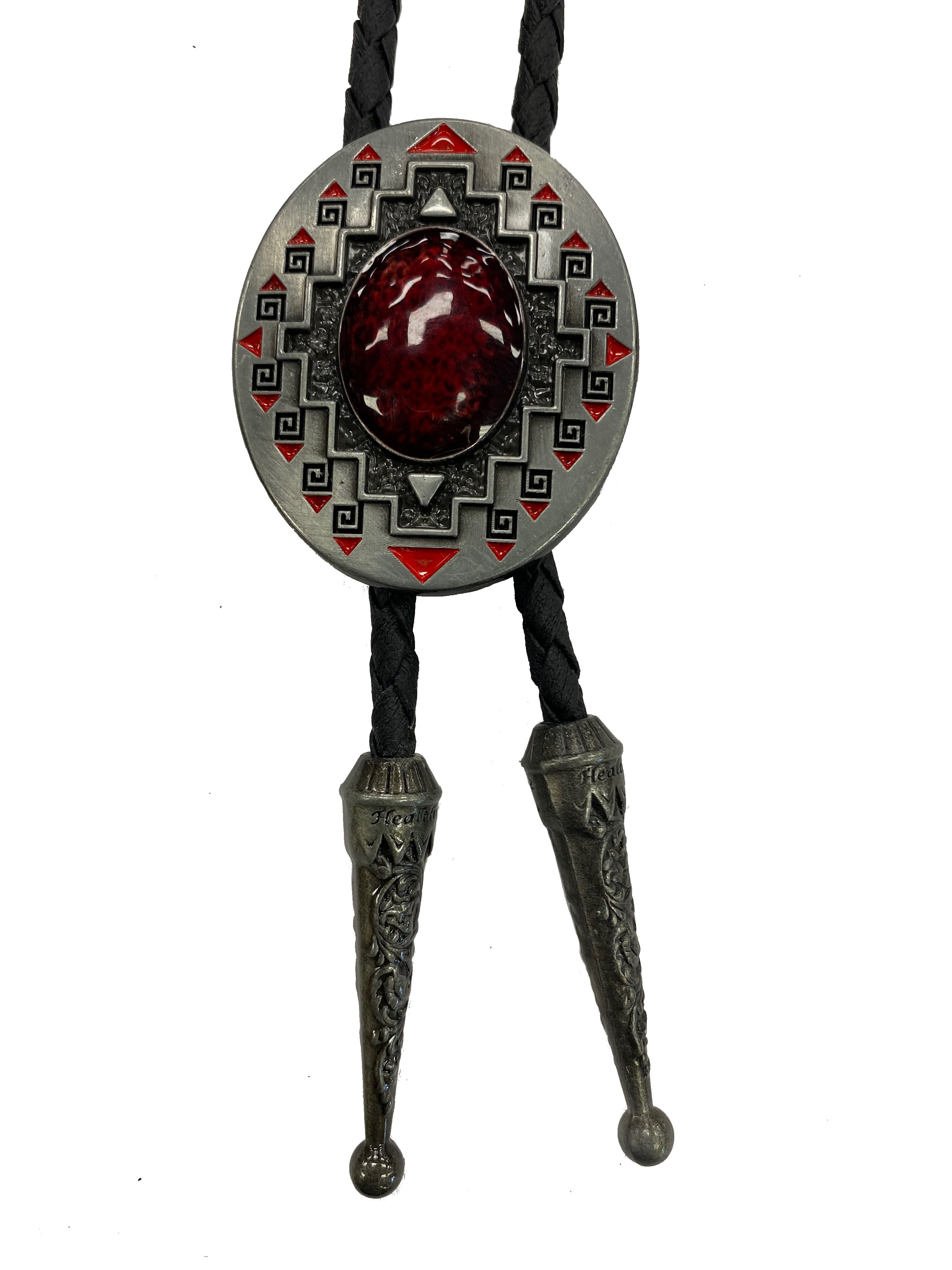 Oval bolo tie featuring geometric patterns and a prominent Red stone in the center, attached to a black braided cord with two metal tips.