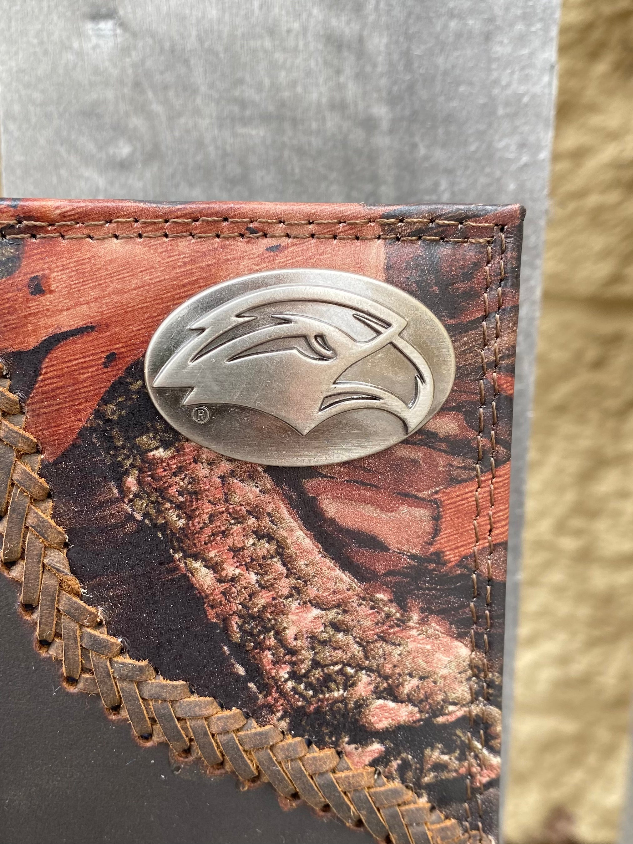 Closeup of Zep-Pro University of Southern Mississippi Golden Eagles 1/2 Mossy Oak Camo/Brown Leather Tall Wallet shows the Golden Eagle logo oval brass concho detail on camo on top right.