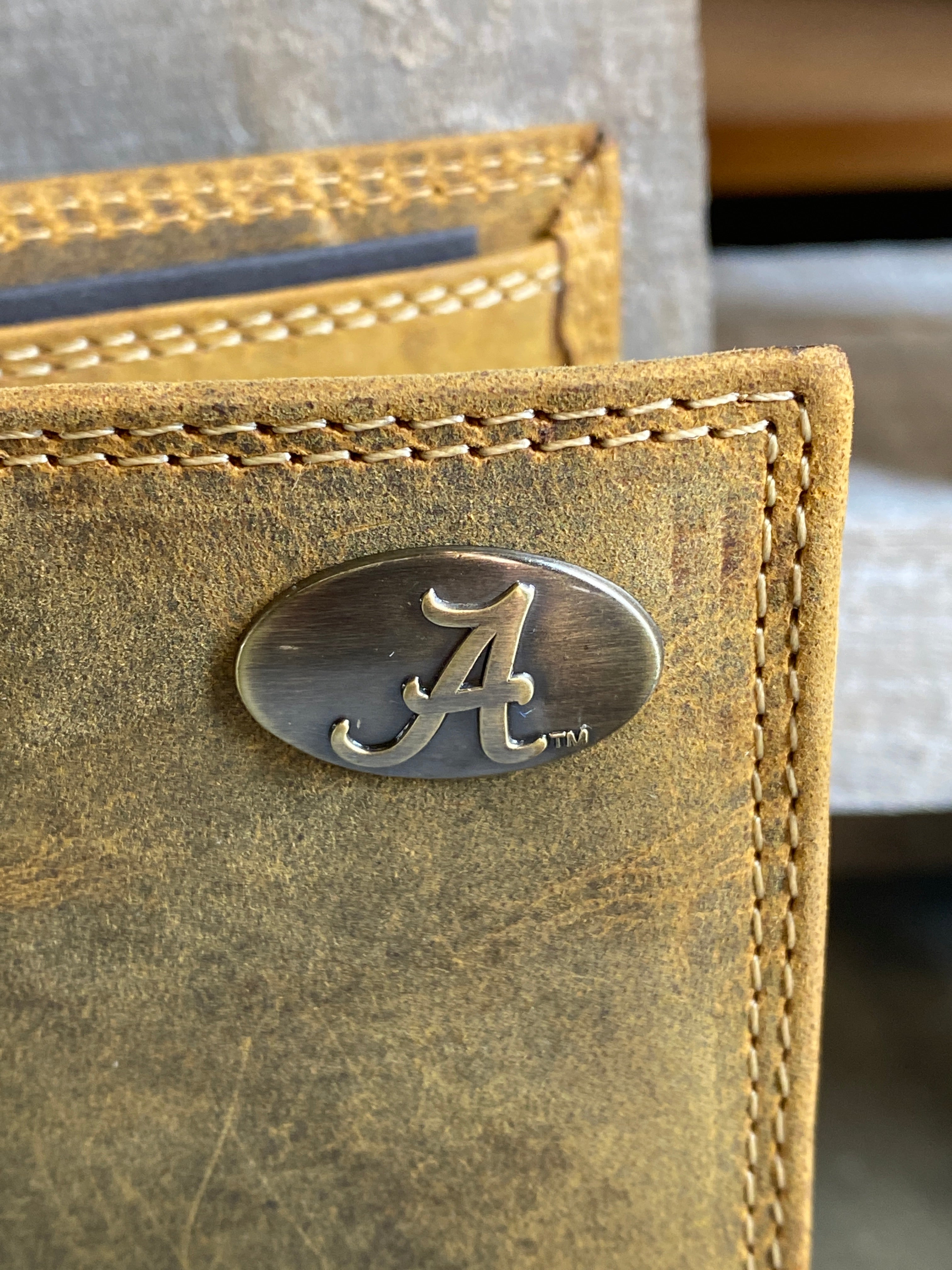 Zep Pro University of Alabama Roll Tide Vintage Tan Leather Bi-fold Wallet. Front view shows close up of Alabama "A" logo concho on upper right corner of wallet.