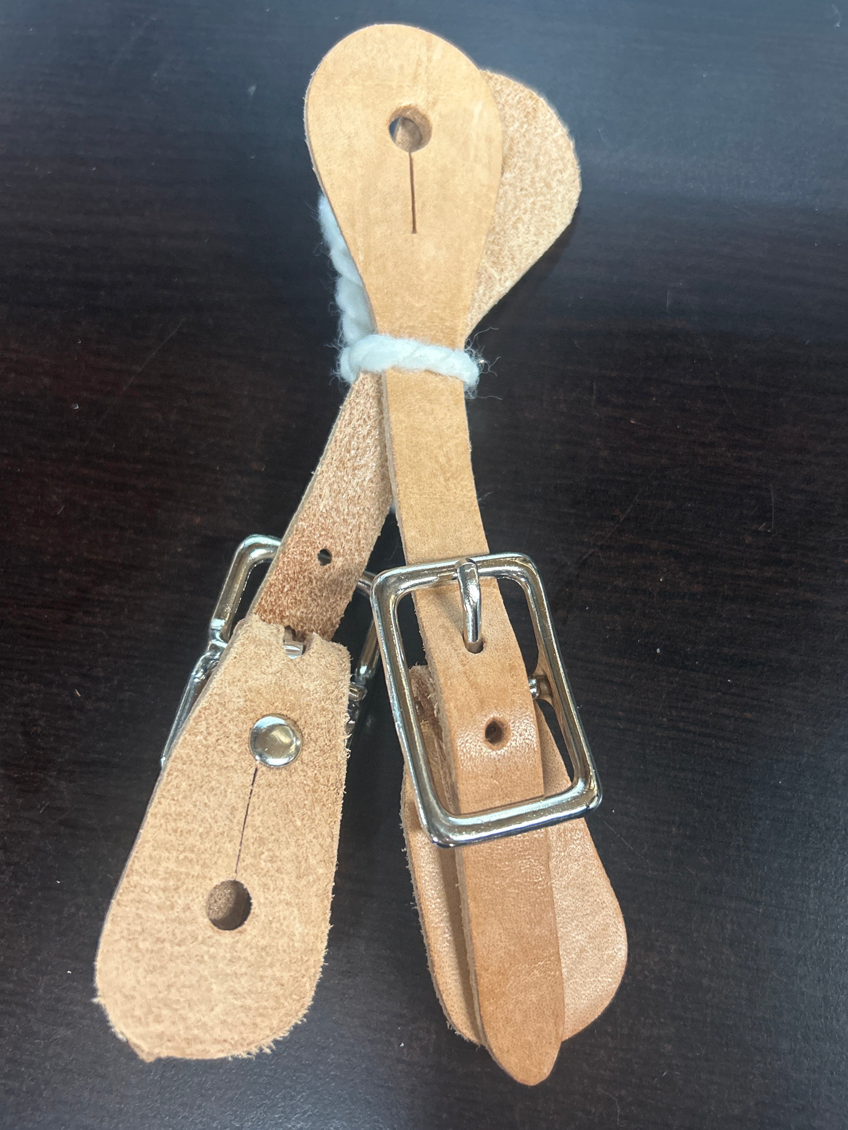 A pair of brown leather spur straps with a metal buckle designed for children's boots.