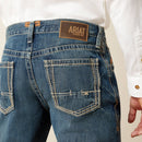 Men's Ariat M4 relaxed fit boot cut jeans in a medium wash. Rear view showing stitching details on pockets and Ariat Denim tag on waist. 