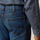 Men's Ariat Fr M4 relaxed fit boot cut jeans in a dark wash. Rear view showing close up of back pocket stitching details and Ariat FR logo tag. 