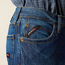 Men's Ariat Fr M4 relaxed fit boot cut jeans in a dark wash. Close up view of front pocket stitching details and Ariat FR logo tag.
