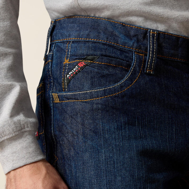 Men's Ariat FR M4 relaxed boot cut jeans in a dark wash. Close up view of side pocket details showing slanted Ariat FR tag. 