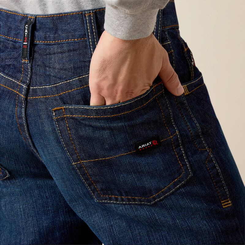 Men's Ariat FR M4 relaxed boot cut jeans in a dark wash. Rear view showing back pocket stitching details and a Ariat FR tag on pocket. 
