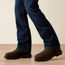 Men's Ariat FR M4 relaxed boot cut jeans in a dark wash. Bottom view showing leg opening over boots. 