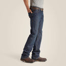 Men's Ariat FR M4 relaxed boot cut jeans in a dark wash. Side view showing jeans on model and leg opening over boots. 