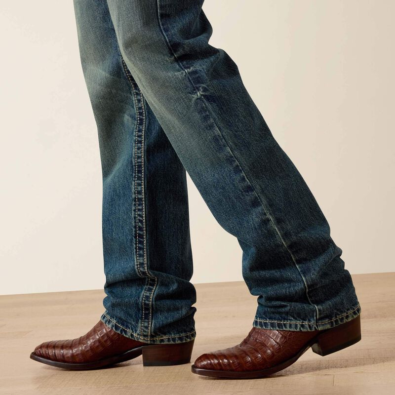 Men's Ariat M5 slim fit straight leg jean in a medium wash. Bottom view showing leg opening over jeans. 