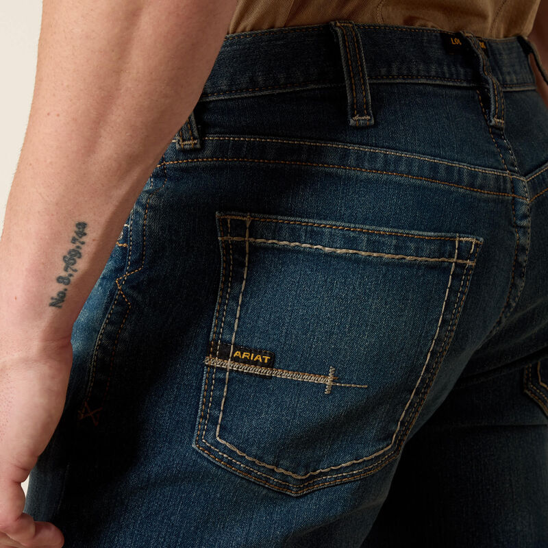 Men's Ariat Rebar straight leg work jeans in a dark wash. Rear view showing a close up of the back pocket featuring stitching and a Ariat logo tag. 