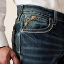 Men's Ariat M4 relaxed fit boot cut jeans in a medium wash. Close up view showing front pocket stitching and slanted Ariat logo tag. 