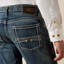 Men's Ariat M4 relaxed fit boot cut jeans in a medium wash . Rear view showing stitching details on back pockets and Ariat logo tag on waist. 