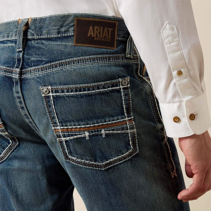 Men's Ariat M4 relaxed fit boot cut jeans in a medium wash . Rear view showing stitching details on back pockets and Ariat logo tag on waist. 
