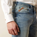 Men's Ariat M4 relaxed fit boot cut jean in a light wash. Close up view of front pockets showing stitch details and slanted Ariat logo tag. 