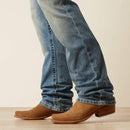 Men's Ariat M4 relaxed fit boot cut jean in a light wash. Bottom view showing leg opening over boots. 