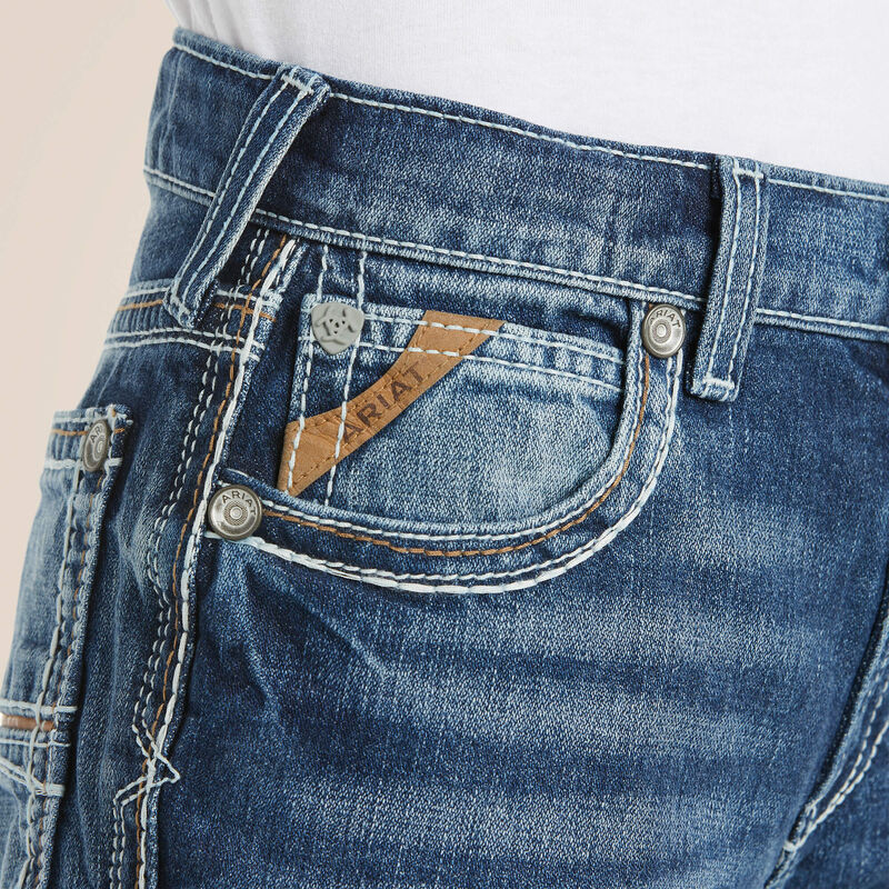 Boys Ariat B4 relaxed fit boot cut jeans in a medium wash. Close up of front pocket details showing stitching and slanted Ariat logo tag. 