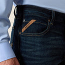 Men's Ariat M5 straight leg jeans in a dark wash. Close up view of front pocket showing slanted Ariat logo tag. 