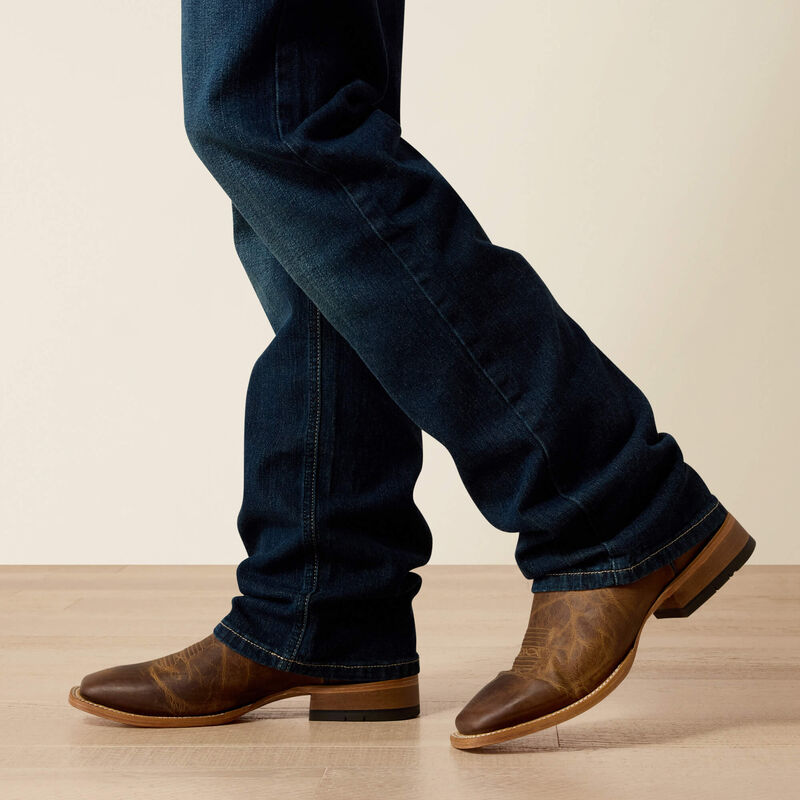Men's Ariat M5 straight leg jeans in a dark wash. Bottom view showing leg opening over boots. 