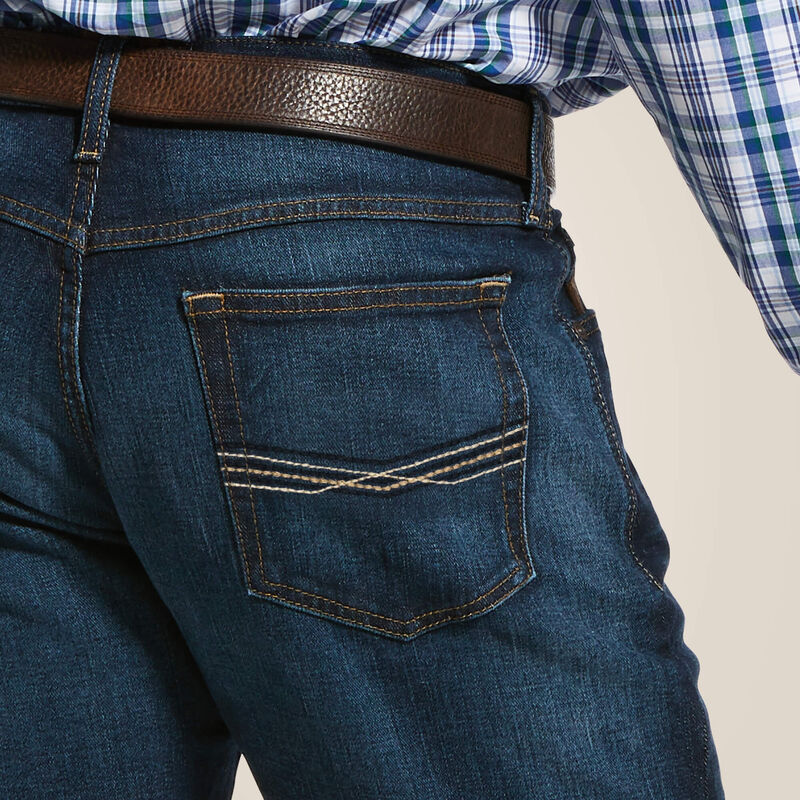 Men's Ariat M5 straight leg jeans in a dark wash. Close up view of stitch details on back pocket. 