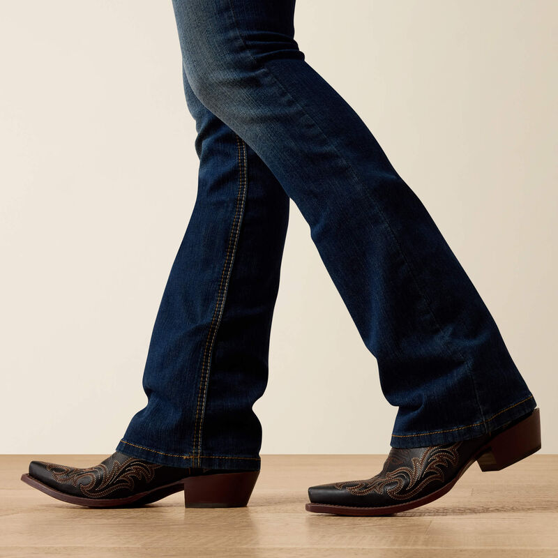 Women's Ariat perfect rise boot cut jeans in a dark wash. Bottom view showing jean opening over boots. 