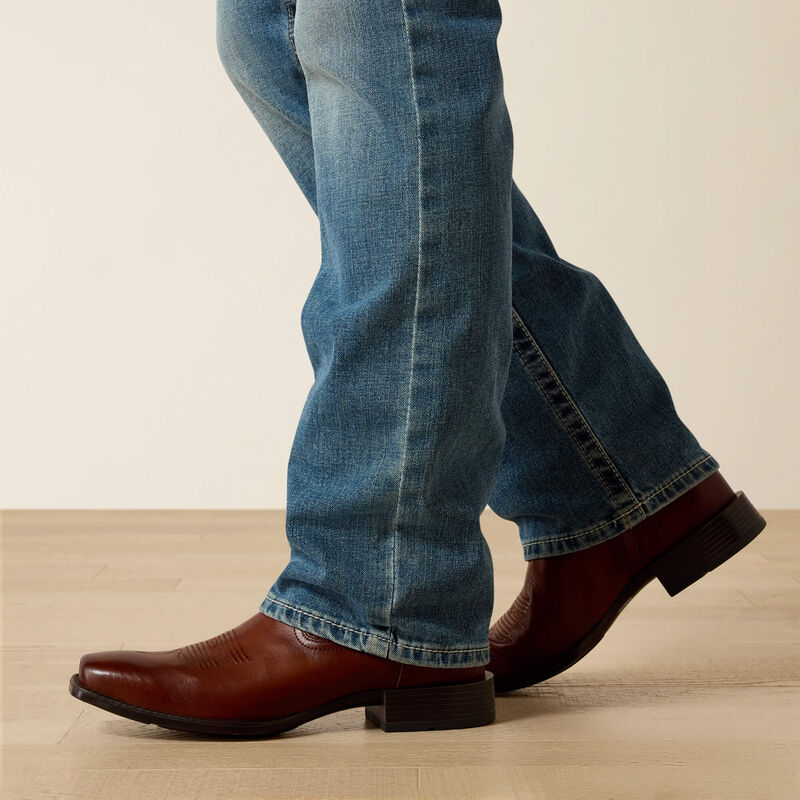 Men's Ariat M7 slim fit straight leg jeans in a light wash. Bottom view showing jeans opening over boots. 