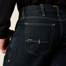 Men's Ariat Rebar M7 slim straight work jeans, in Blackstone a dark wash. Rear view showing back pocket stitching with Ariat logo. Also shows side stitching and anchored belt loops. 