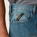 Men's Ariat M5 Rebar work jeans in Edgewood, a light wash. Close up of front pocket details including a knife pocket and a Ariat logo tag. 