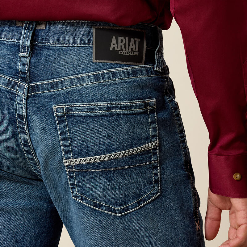 Men's Ariat M4 relaxed fit boot cut jean in a medium wash. Rear view showing close up of pocket stitching details and Ariat Denim logo patch. 