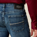 Men's Ariat M4 relaxed fit boot cut jean in a medium wash. Rear view showing close up of pocket stitching details and Ariat Denim logo patch. 
