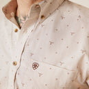 Men's Ariat long sleeve button down shirt in Bandshell, a tan color with a print of steer skulls. Close up of left chest pocket showing Ariat shield logo and the button down collar. 