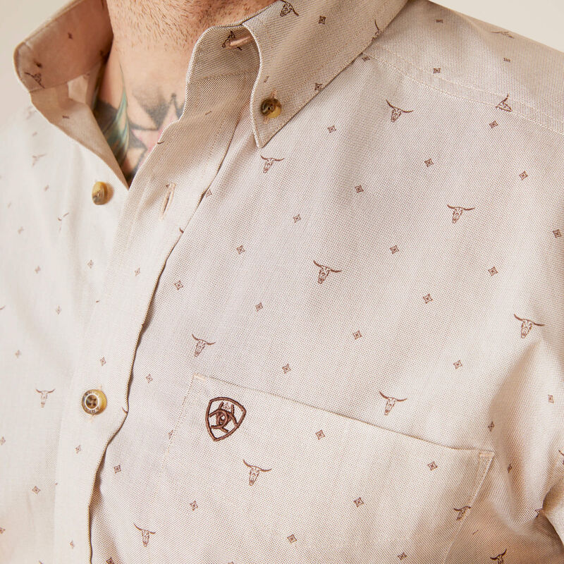Men's Ariat long sleeve button down shirt in Bandshell, a tan color with a print of steer skulls. Close up of left chest pocket showing Ariat shield logo and the button down collar. 
