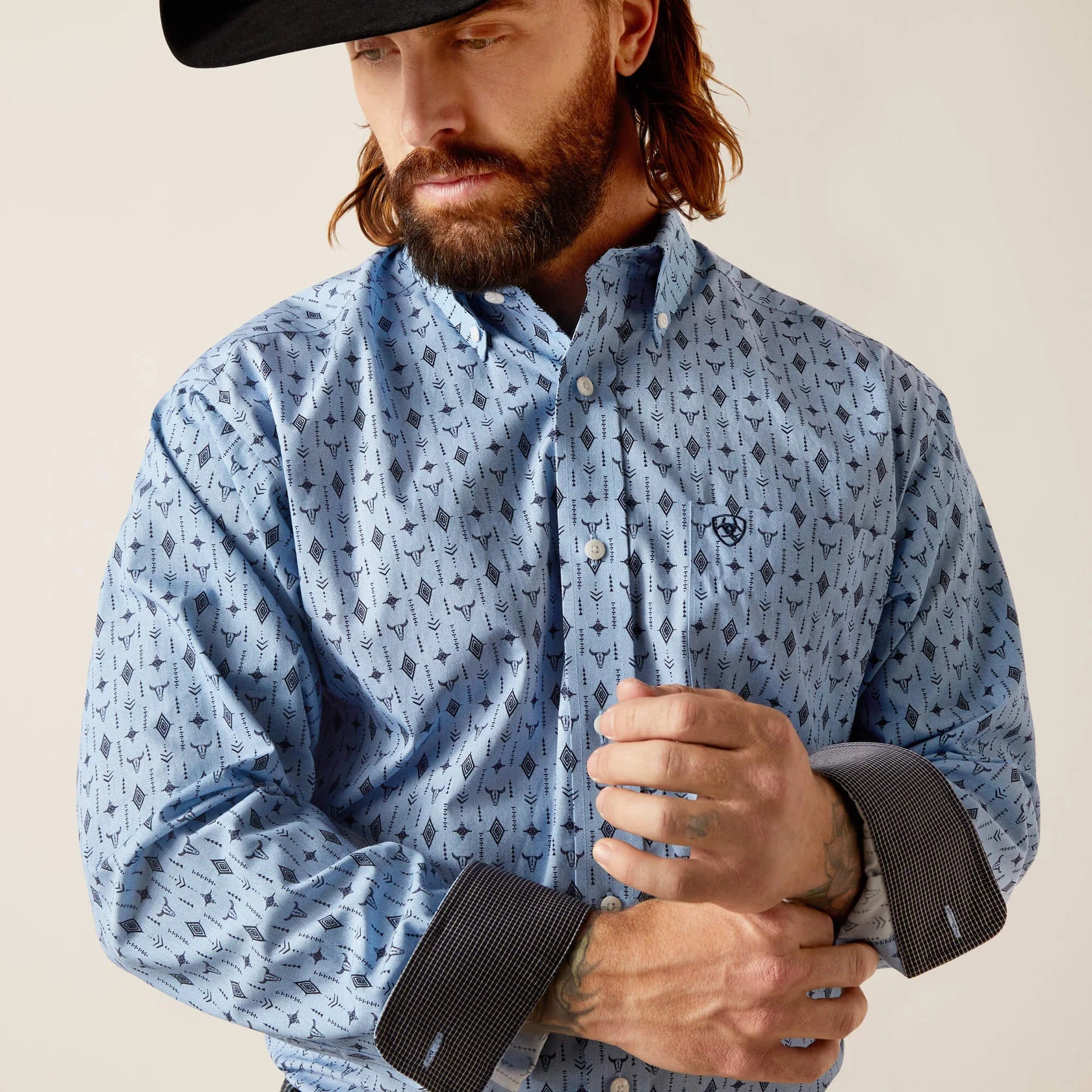 Men's Ariat Light Blue long sleeve shirt with a western print of steer head and geometric shapes. Close up of contrast pattern inside cuffs and Ariat shield logo stitched on left chest pocket. 